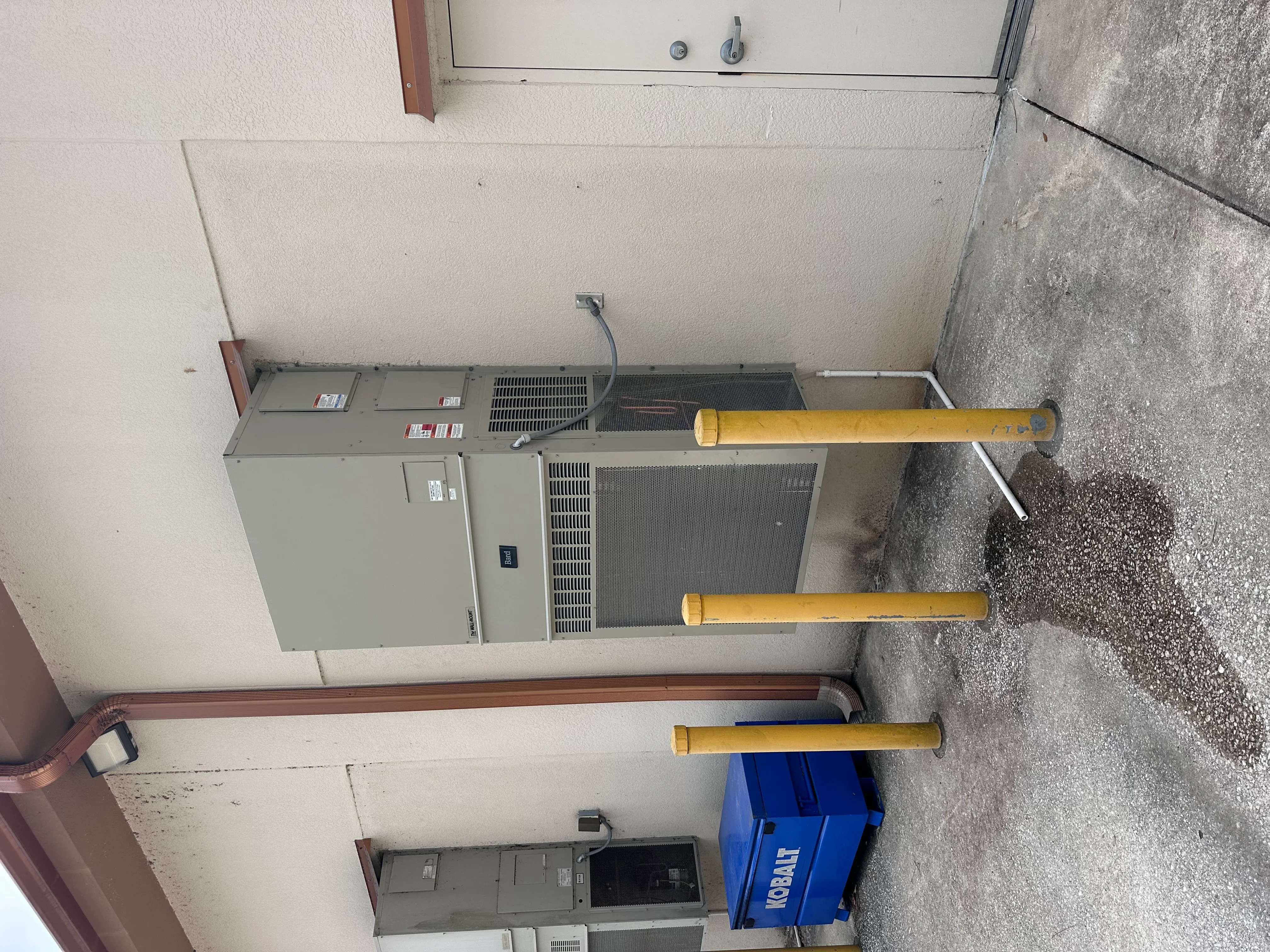 Commercial HVAC units with yellow refrigerant lines and ductwork installed on concrete pad