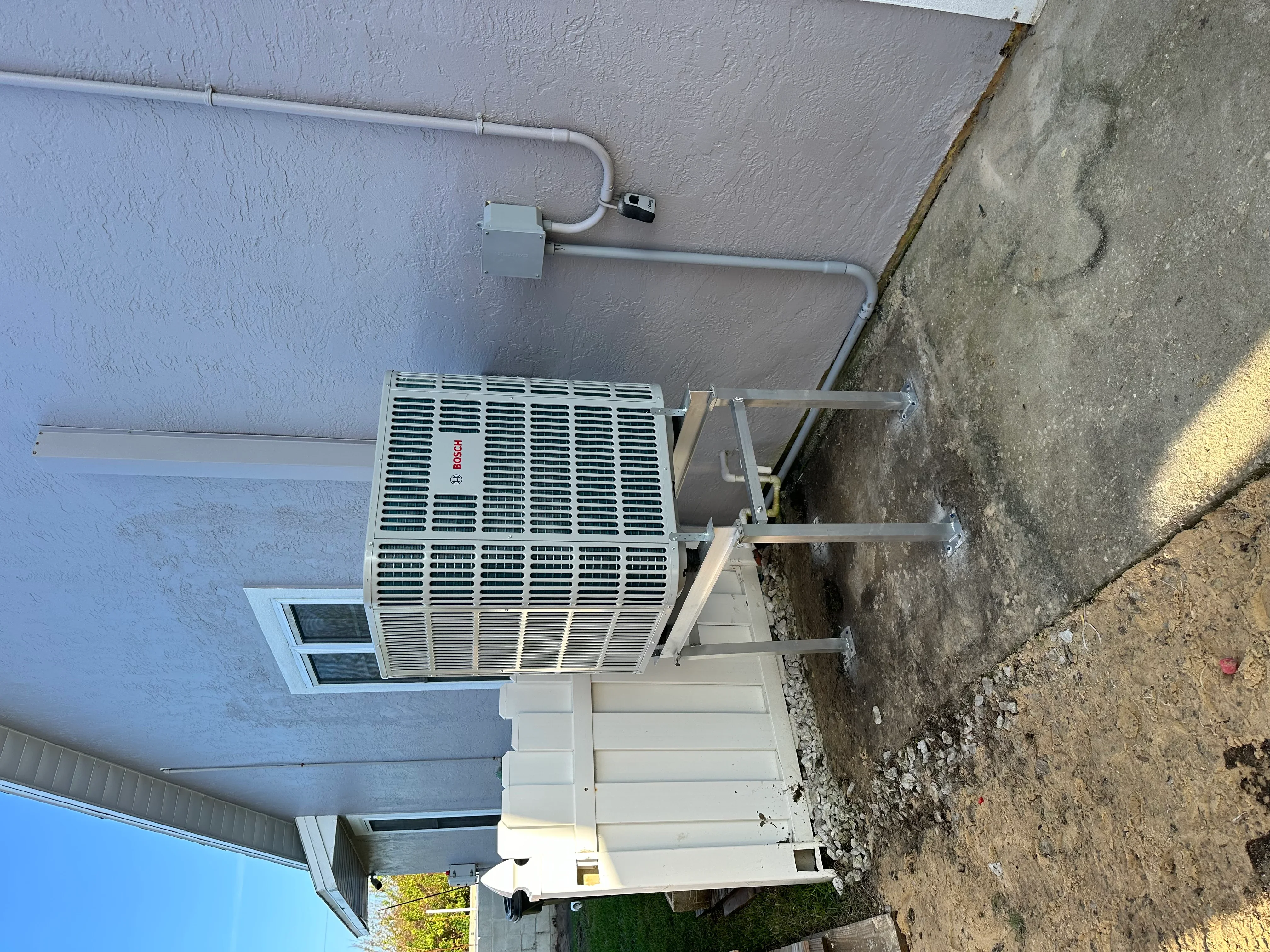 Bosch heat pump unit mounted on stucco wall with metal support brackets and refrigerant lines