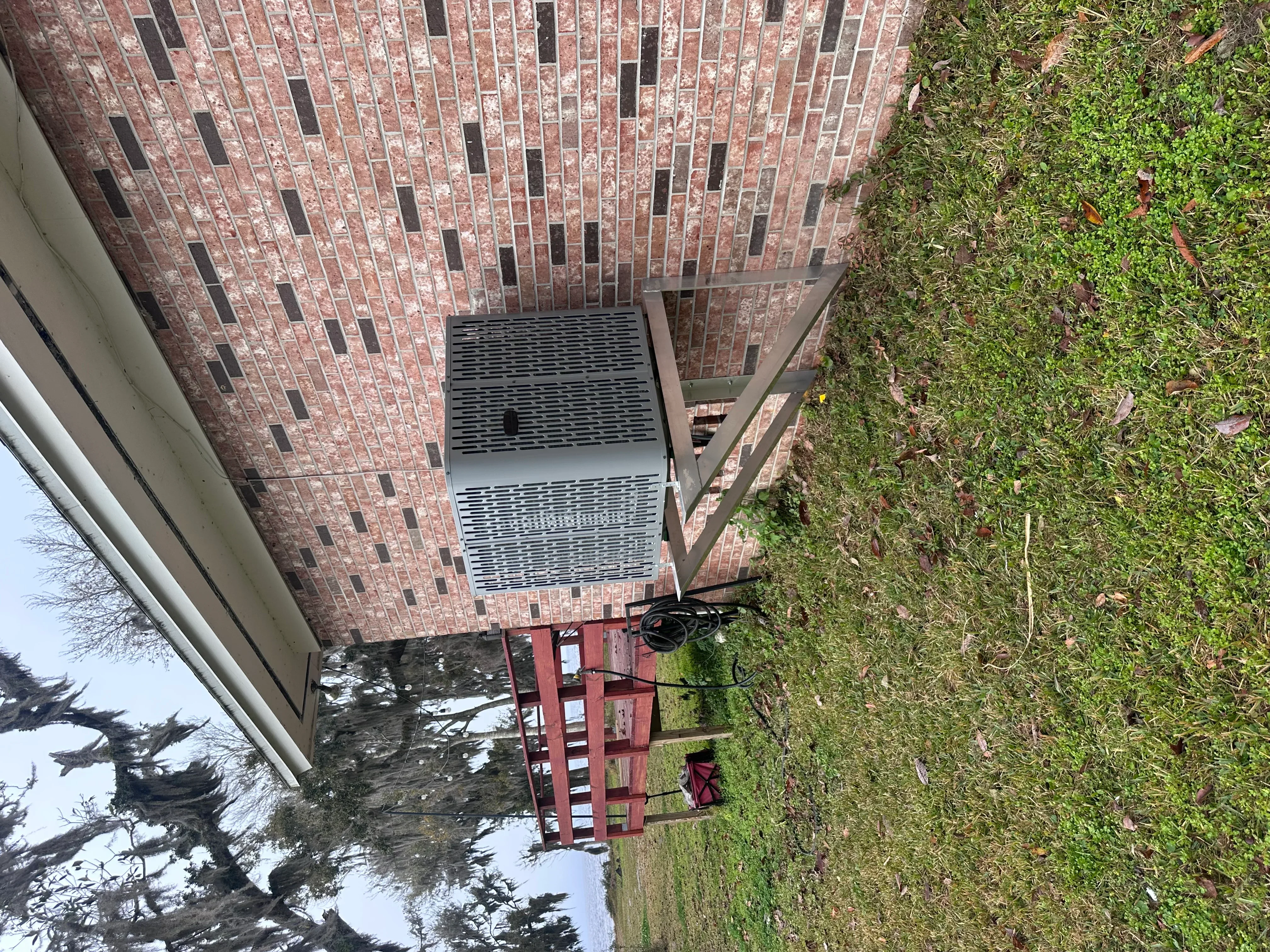 Outdoor AC condenser unit installed on brick home exterior with metal mounting bracket
